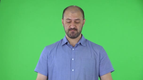 Portret van mannen van middelbare leeftijd die naar de camera kijken en onverschillig in haar handen klappen. Kalende man met een baard in een blauw shirt poserend op een groen scherm in de studio. Sluiten.. — Stockvideo