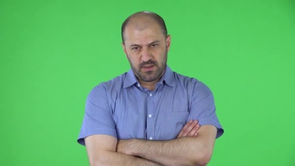 Retrato de un hombre de mediana edad mirando a la cámara con expresión frustrada y cansada, con los brazos cruzados sobre el pecho. Hombre calvo con barba en camisa azul posando en pantalla verde en el estudio. De cerca.. — Vídeo de stock