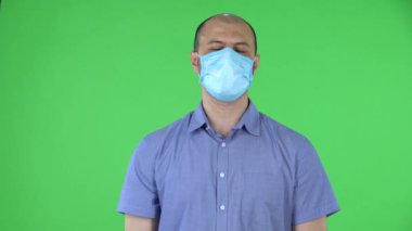 Medikal maskeli orta yaşlı bir adamın portresi dikkatle dinliyor, onaylayarak başını sallıyor, parmağıyla işaret ediyor evet, haklısın. Stüdyoda yeşil ekranda kel erkek poz veriyor. Kapat..