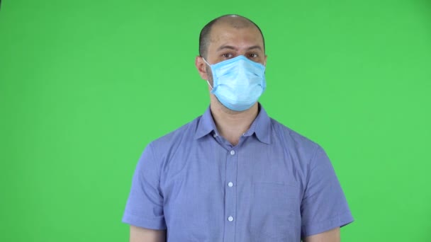 Retrato de un hombre de mediana edad con máscara médica muestra un gesto de brazos cruzados que significa no. Hombre calvo con camisa azul posando en pantalla verde en el estudio. De cerca.. — Vídeos de Stock