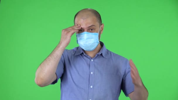 의료용 마스크를 쓰고 있는 중년 남자의 모습이 걱정되어 당황하였다. 파란색 셔츠를 입은 남자가 스튜디오의 녹색 화면에 포즈를 취하고 있습니다. 닫아. — 비디오
