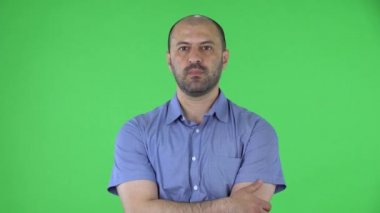 Kameraya bakan orta yaşlı bir adamın portresi zaferi kutluyor. Mavi gömlekli kel erkek stüdyoda yeşil ekranda poz veriyor. Kapat..