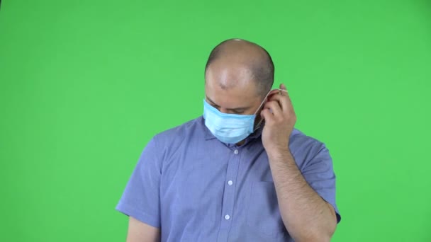 Портрет мужчины средних лет снимает медицинскую маску и вздыхает с облегчением. Лысый мужчина в синей рубашке позирует на зеленом экране в студии. Закрыть. — стоковое видео