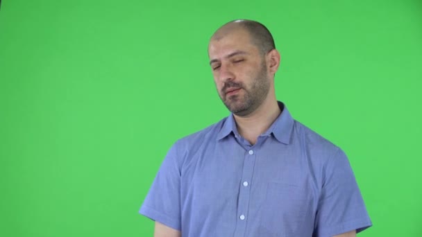 Портрет мужчины средних лет, смотрящего вокруг и делающего тайный жест молчания. Лысый мужчина с бородой в синей рубашке позирует на зеленом экране в студии. Закрыть. — стоковое видео