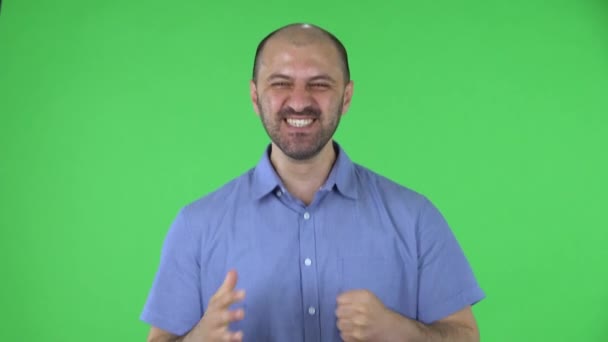 Πορτρέτο ενός μεσήλικα άνδρες κοιτάζοντας την κάμερα χαίρεται και γιορτάζει τη νίκη. Φαλακρός άντρας με γενειάδα σε μπλε πουκάμισο που ποζάρει σε πράσινη οθόνη στο στούντιο. Κλείσε.. — Αρχείο Βίντεο