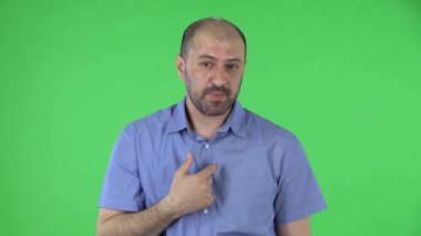 Orta yaşlı bir adamın portresi kameraya bakıyor, başını sallıyor, masumiyetini gösteriyor. Mavi gömlekli kel erkek stüdyoda yeşil ekranda poz veriyor. Kapat..