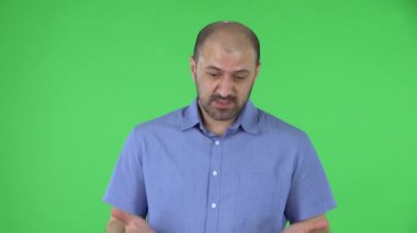 Öfkeyle kameraya bakan orta yaşlı bir adamın portresi ellerini sallıyor, nasıl da omuz silkiyor. Mavi gömlekli kel erkek stüdyoda yeşil ekranda poz veriyor. Kapat..