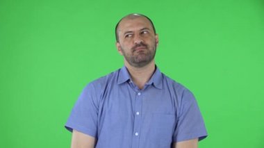 Kameraya bakan orta yaşlı bir adamın portresi iki eliyle baş parmak işareti gösteriyor. Mavi gömlekli kel erkek stüdyoda yeşil ekranda poz veriyor. Kapat..