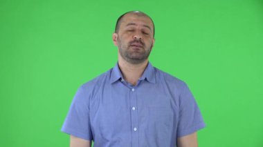 Kameraya bakan orta yaşlı bir adamın portresi işaret parmaklarını gösteriyor. Mavi gömlekli kel erkek stüdyoda yeşil ekranda poz veriyor. Kapat..