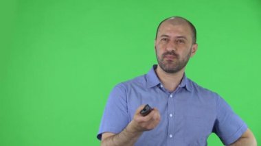 Elinde televizyon kumandası olan orta yaşlı bir adamın portresi kanalları değiştiriyor. Mavi gömlekli kel erkek stüdyoda yeşil ekranda poz veriyor. Kapat..