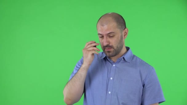 Portret van een man van middelbare leeftijd die met concentratie in de camera kijkt, blij dat er een idee is. Kalende man met baard in blauw shirt poserend op groen scherm in de studio. Sluiten.. — Stockvideo