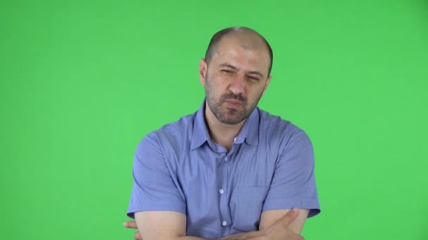 Portrét muže středního věku, který se soustředěně dívá do kamery a pak se rozčiluje. Plešatý muž s vousy v modré košili pózující na zelené obrazovce ve studiu. Zavřít. — Stock video