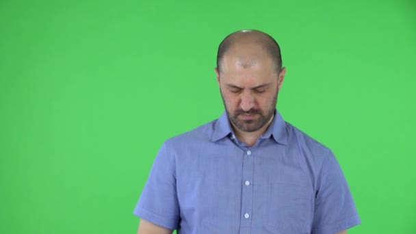 Портрет мужчины средних лет расстроен и устал. Лысый мужчина с бородой в синей рубашке позирует на зеленом экране в студии. Закрыть. — стоковое видео