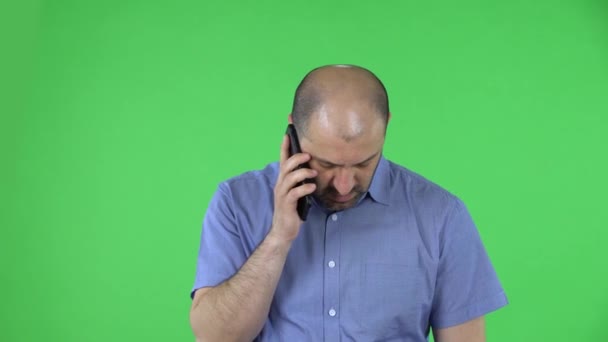 Retrato de um homem de meia-idade falando em seu smartphone. Homem careca com barba em camisa azul posando na tela verde no estúdio. Fechar. — Vídeo de Stock