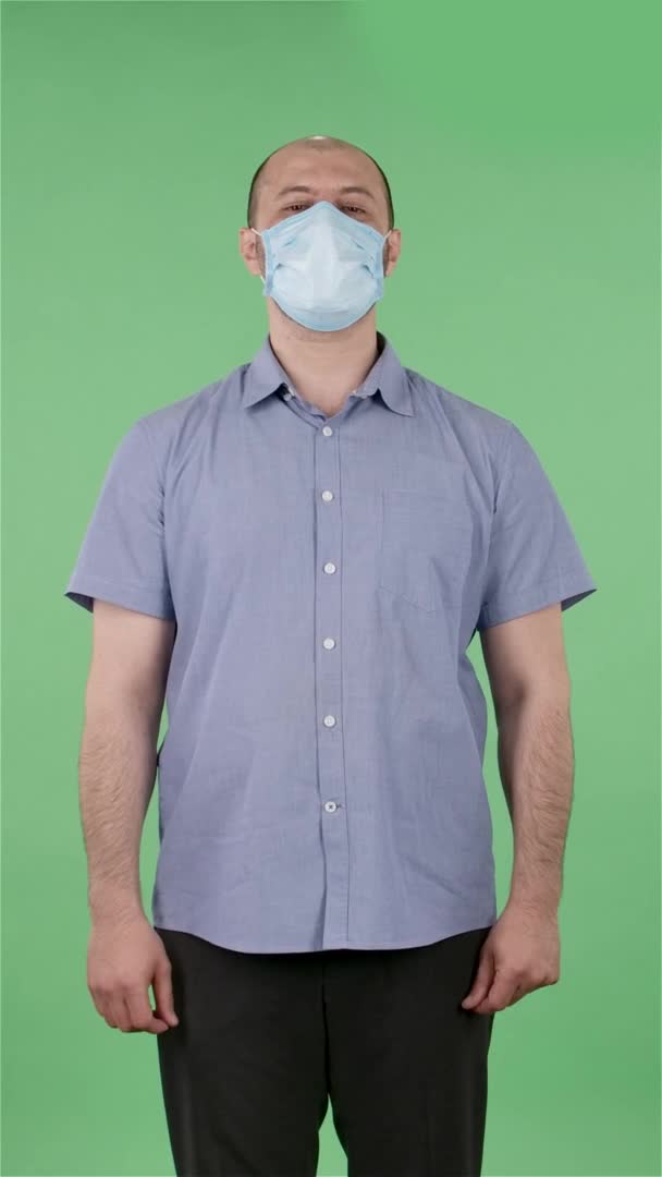 Портрет мужчины средних лет в медицинской маске возмущения машет руками, пожимает плечами, как это. Лысый мужчина позирует на зеленом экране в студии. Медленное движение. Вертикальное видео. — стоковое видео