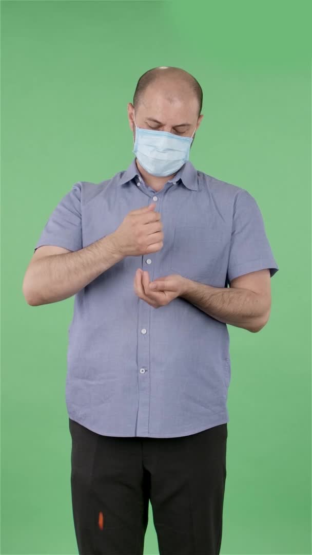 Портрет мужчины средних лет в медицинской маске изливает лекарство из рук в руки. Лысый мужчина в синей рубашке позирует на зеленом экране в студии. Медленное движение. Вертикальное видео. — стоковое видео
