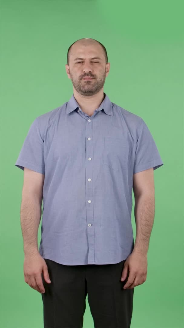 Портрет мужчины средних лет, смотрящего в камеру. Лысый мужчина с бородой в синей рубашке позирует на зеленом экране в студии. Медленное движение. Вертикальное видео. — стоковое видео