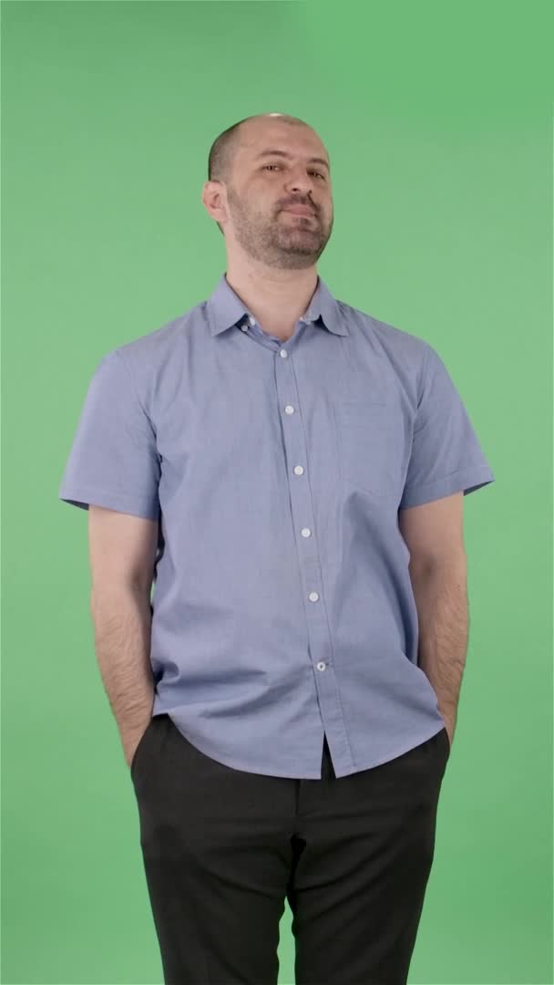 Portrait d'un homme d'âge moyen regardant ludique la caméra et faisant un geste cardiaque et soufflant un baiser. Homme chauve avec barbe posant sur écran vert en studio. Au ralenti. Vidéo verticale. — Video