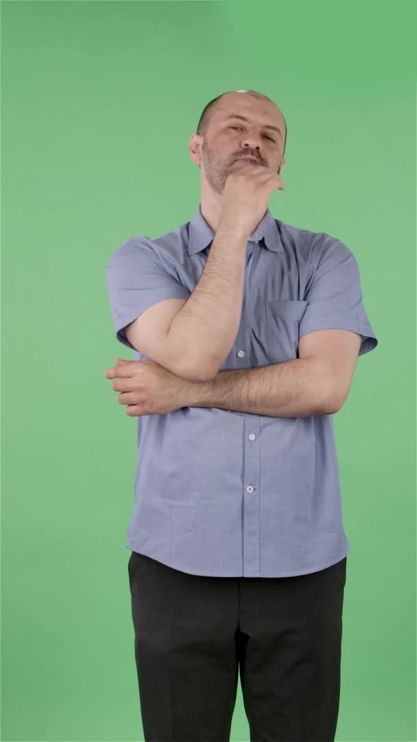 Portrait d'un homme d'âge moyen regardant la caméra et pensant avec concentration. Homme chauve avec barbe en chemise bleue posant sur écran vert en studio. Au ralenti. Vidéo verticale. — Video