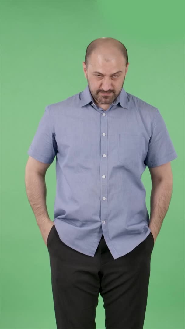 Portrét muže středního věku, který se dívá přímo do kamery, říká "Jejda" a "zmatený". Plešatý muž s vousy v modré košili pózující na zelené obrazovce ve studiu. Zpomal. Svislé video. — Stock video