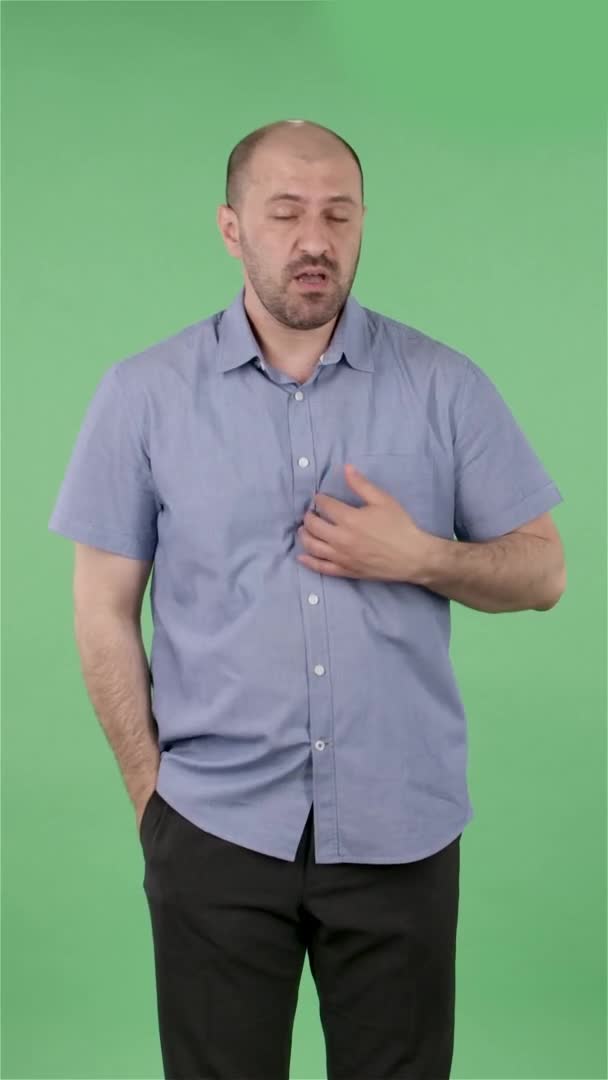 Ritratto di un uomo di mezza età che guarda la telecamera scuotere la testa, esprimendo la sua innocenza. Maschio calvo con barba in camicia blu in posa sullo schermo verde in studio. Al rallentatore. Video verticale. — Video Stock