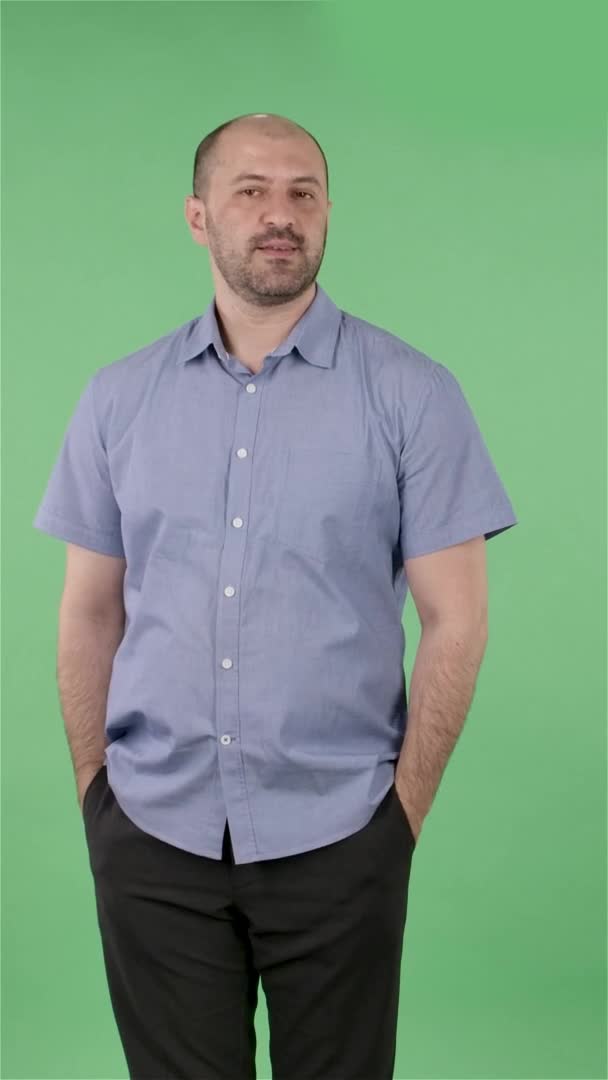 Retrato de un hombre de mediana edad llamando a alguien. Hombre calvo con barba en camisa azul posando en pantalla verde en el estudio. En cámara lenta. Vídeo vertical. — Vídeos de Stock