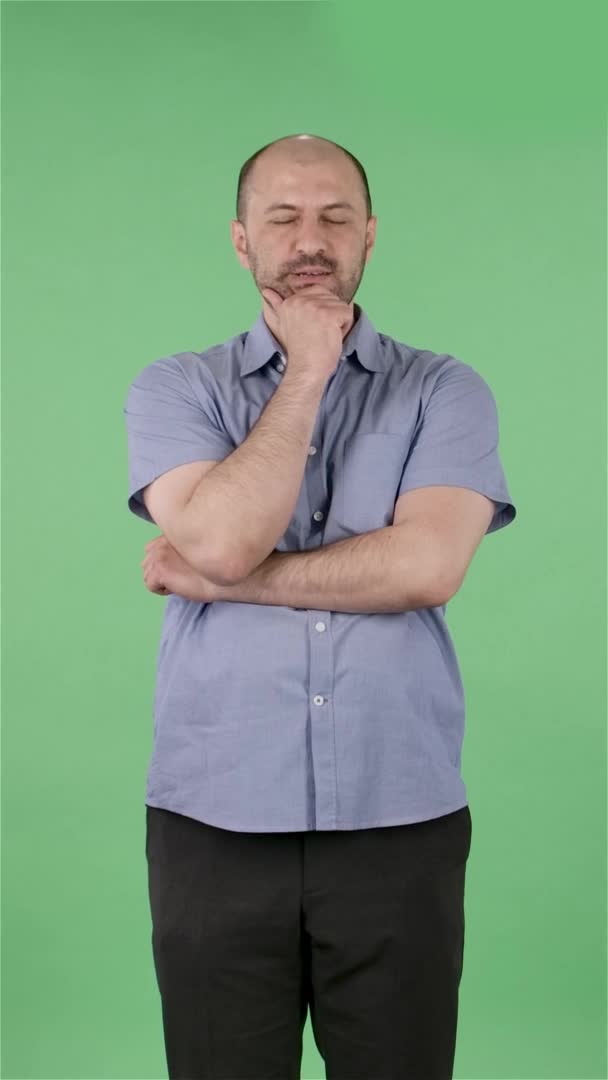 Πορτρέτο ενός μεσήλικου άντρα που κοιτάζει την κάμερα με αγανάκτηση κουνάει τα χέρια του. Φαλακρός άντρας με γενειάδα σε μπλε πουκάμισο που ποζάρει σε πράσινη οθόνη στο στούντιο. Αργή κίνηση. Κάθετη βίντεο. — Αρχείο Βίντεο
