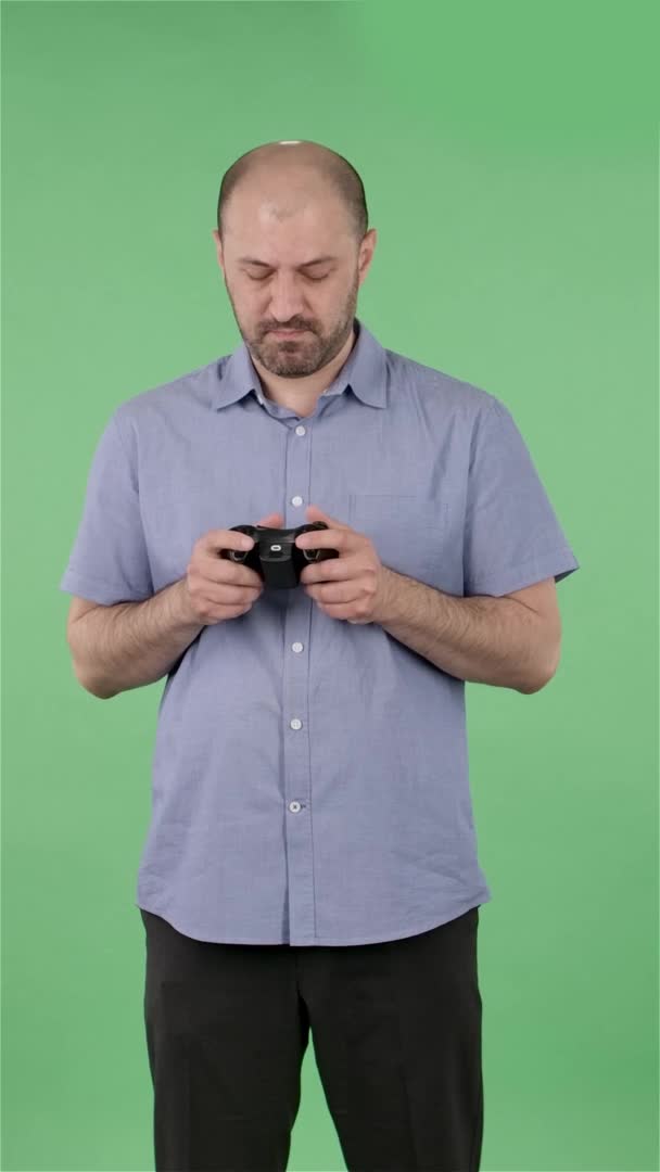 Retrato de un hombre de mediana edad jugando un videojuego usando un controlador inalámbrico con alegría y regocijo. Hombre calvo con barba posando en pantalla verde en el estudio. En cámara lenta. Vídeo vertical. — Vídeo de stock