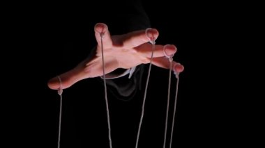 Kuklayı kontrol etmek için parmaklarında ipler olan takım elbiseli bir diktatörün eli. Siyah izole edilmiş arka planda kukla dizileriyle erkek elini kapat. Yavaş çekim.
