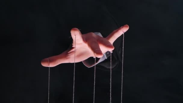 Hand van dictator in een zakenpak met touwtjes aan de vingers om de marionet te controleren. Close-up mannelijke hand met snaren van marionetten op rook zwarte geïsoleerde achtergrond. Langzame beweging. — Stockvideo