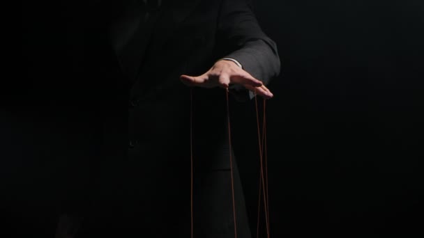 Puppet Master ελέγχει και χειρίζεται τις μαριονέτες με χορδές που συνδέονται με τα δάχτυλά του. Το χέρι του επιχειρηματία με κουστούμι ελέγχει τη μοίρα των ανθρώπων. Απομονωμένο σε μαύρο φόντο. Αργή κίνηση. — Αρχείο Βίντεο