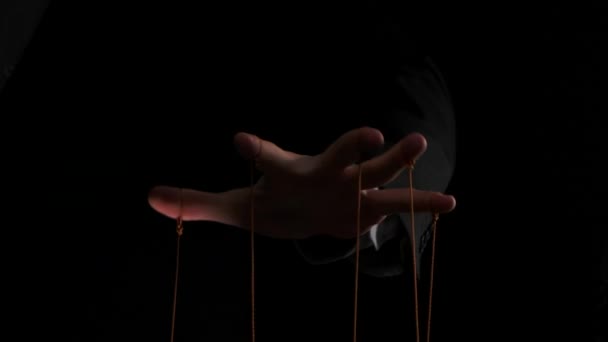 Puppet Master controls and manipulates the puppets with strings attached to his fingers. Hand of businessman in a suit close up controls destinies of people. Isolated on black background. Slow motion. — Stock Video