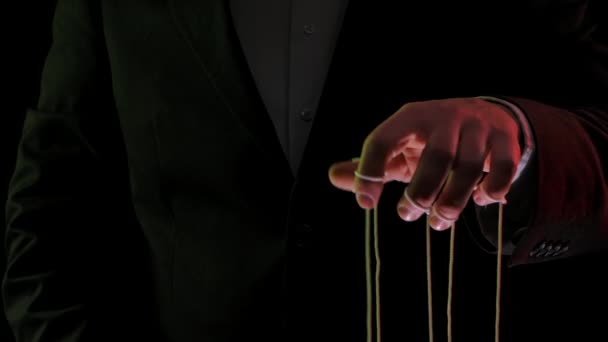 Geschäftsmann im Anzug manipuliert die Fäden von Marionetten, die an seinen Fingern befestigt sind. Herrschaft, Macht und Unterwerfung. Nahaufnahme der Hände, die mit farbigen Lichtern beleuchtet sind. Zeitlupe. — Stockvideo