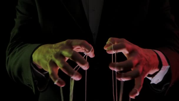 O líder do empresário em um terno manipula as cordas de fantoches amarradas aos dedos. Dominação, poder e conceito de submissão. Mãos de homem fechadas iluminadas com luzes coloridas. Movimento lento. — Vídeo de Stock