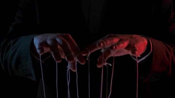 Burattinaio che manipola e tira fili di marionette. Mani maschili da vicino dipinte con luci colorate su sfondo nero. Le persone sono giocattoli nelle mani di un dittatore dominante. Rallentatore. — Video Stock