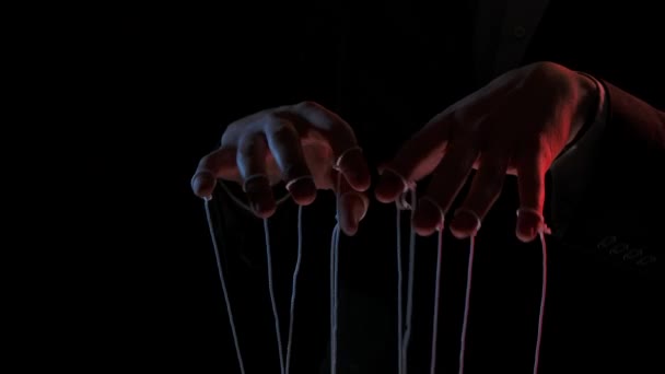 Burattinaio che manipola e tira fili di marionette. Mani maschili da vicino dipinte con luci colorate su sfondo nero. Le persone sono giocattoli nelle mani di un dittatore dominante. Rallentatore. — Video Stock