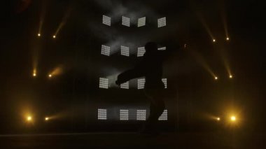 Yetenekli genç bir hip hop dansçısının silueti. Karanlık bir stüdyoda, dumanlı ve neon ışıklı bir sahnede hip hop sokak dansı. Dinamik ışıklandırma efektleri. Yaratıcı yetenekler. Yavaş çekim.