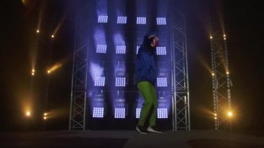 Yetenekli genç bir hip hop dansçısının silueti. Karanlık bir stüdyoda, dumanlı ve neon ışıklı bir sahnede hip hop sokak dansı. Dinamik ışıklandırma efektleri. Yaratıcı yetenekler. Yavaş çekim.