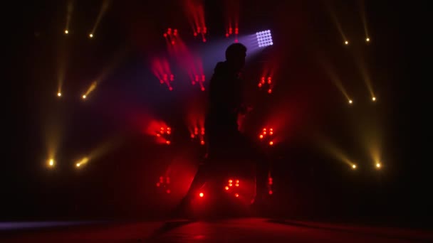 Silhouet van een getalenteerde jonge hiphopdanser. Hip hop straat dans op een podium in donkere studio met rook en neon verlichting. Dynamische lichteffecten. Creatieve vaardigheden. Langzame beweging. — Stockvideo