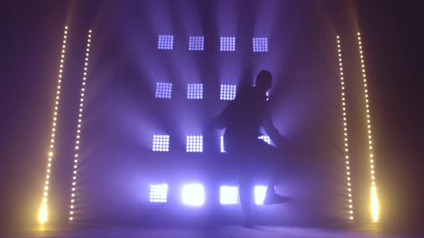 Silhouette of a talented young hip hop dancer. Hip hop street dance on a stage in dark studio with smoke and neon lighting. Dynamic lighting effects. Creative skills. Slow motion. — Stock Video