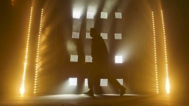 Yetenekli genç bir hip hop dansçısının silueti. Karanlık bir stüdyoda, dumanlı ve neon ışıklı bir sahnede hip hop sokak dansı. Dinamik ışıklandırma efektleri. Yaratıcı yetenekler. Yavaş çekim.