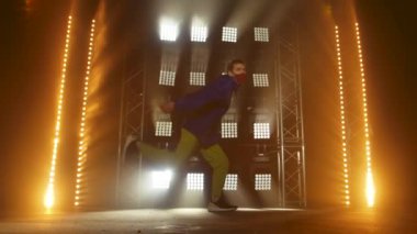 Yetenekli genç bir hip hop dansçısının silueti. Karanlık bir stüdyoda, dumanlı ve neon ışıklı bir sahnede hip hop sokak dansı. Dinamik ışıklandırma efektleri. Yaratıcı yetenekler. Yavaş çekim.