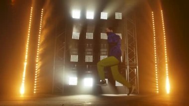 Yetenekli genç bir hip hop dansçısının silueti. Karanlık bir stüdyoda, dumanlı ve neon ışıklı bir sahnede hip hop sokak dansı. Dinamik ışıklandırma efektleri. Yaratıcı yetenekler. Yavaş çekim.