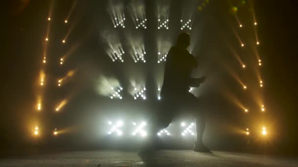 Silhouet van een getalenteerde jonge hiphopdanser. Hip hop straat dans op een podium in donkere studio met rook en neon verlichting. Dynamische lichteffecten. Creatieve vaardigheden. Langzame beweging. — Stockvideo