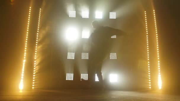 Silhouet van een getalenteerde jonge hiphopdanser. Hip hop straat dans op een podium in donkere studio met rook en neon verlichting. Dynamische lichteffecten. Creatieve vaardigheden. Langzame beweging. — Stockvideo