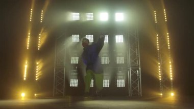 Yetenekli genç bir hip hop dansçısının silueti. Karanlık bir stüdyoda, dumanlı ve neon ışıklı bir sahnede hip hop sokak dansı. Dinamik ışıklandırma efektleri. Yaratıcı yetenekler. Yavaş çekim.