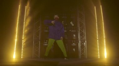 Yetenekli genç bir hip hop dansçısının silueti. Karanlık bir stüdyoda, dumanlı ve neon ışıklı bir sahnede hip hop sokak dansı. Dinamik ışıklandırma efektleri. Yaratıcı yetenekler. Yavaş çekim.