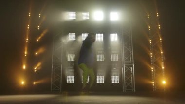 Yetenekli genç bir hip hop dansçısının silueti. Karanlık bir stüdyoda, dumanlı ve neon ışıklı bir sahnede hip hop sokak dansı. Dinamik ışıklandırma efektleri. Yaratıcı yetenekler. Yavaş çekim.