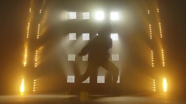 Yetenekli genç bir hip hop dansçısının silueti. Karanlık bir stüdyoda, dumanlı ve neon ışıklı bir sahnede hip hop sokak dansı. Dinamik ışıklandırma efektleri. Yaratıcı yetenekler. Yavaş çekim.