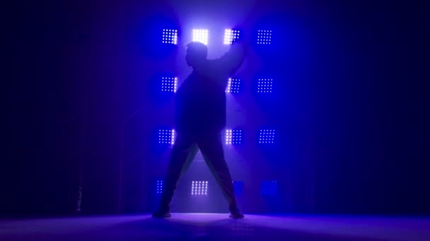 Silhouette of a talented young hip hop dancer. Hip hop street dance on a stage in dark studio with smoke and neon lighting. Dynamic lighting effects. Creative skills. Slow motion. — Stock Video
